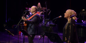 Rob Mathes playing guitar on stage accompanied by a woman singing